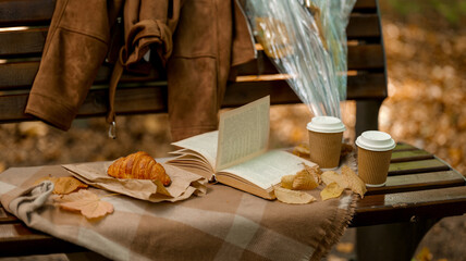 Autumn picnic scene with coffee, a book, and a croissant on a park bench.