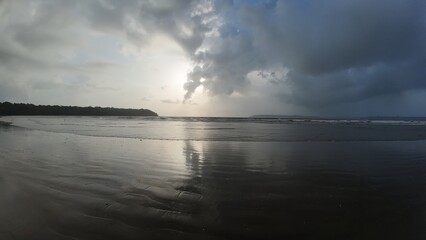 Obraz premium Serene Coastal Sunset with Cloud Reflections on Wet Sand Beach