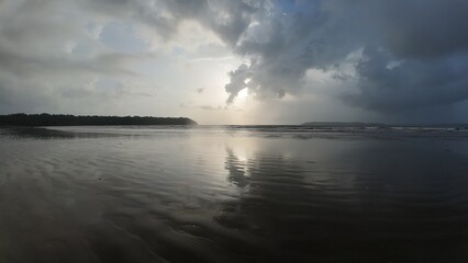 Serene Coastal Sunset with Cloud Reflections on Wet Sand Beach