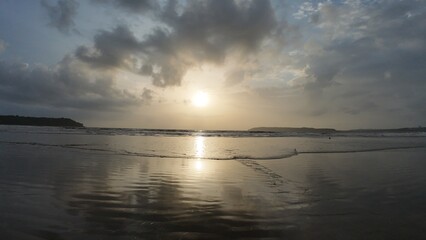 Naklejka premium Idyllic Coastal Sunrise with Gentle Waves, Dramatic Clouds, and Mirror-Like Reflections