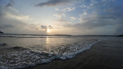 Obraz premium Idyllic Coastal Sunrise with Gentle Waves, Dramatic Clouds, and Mirror-Like Reflections