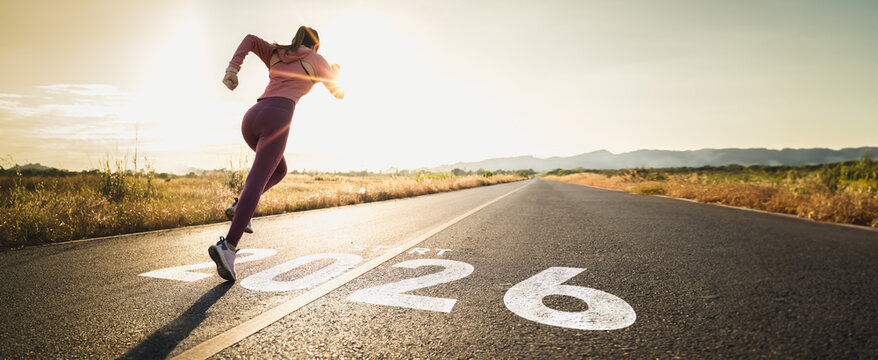 New year 2026 or start straight concept.word 2026 written on the asphalt road and athlete woman runner stretching leg preparing for new year at sunset.Concept of challenge or career path and change.
