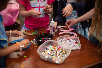 Kid's crafting together with a table full of craft supplies such as pom poms, gems, sparkles, sequins