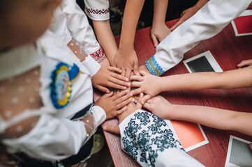 Many Ukrainian children in embroidered shirts gathered in a circle with their hands clasped on each other on the table showing the symbol of victory. Photo, concept.