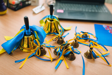 A close-up photo in a Ukrainian school of many bronze, gilded bells with a yellow and blue ribbon on a table. A holiday in Ukraine.