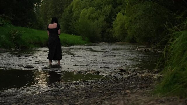 A woman splashes water with her foot in a mountain river in the evening
