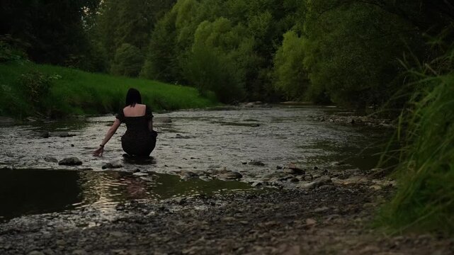 A woman splashes water with her hand in a mountain river in the evening