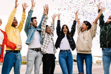 Obraz premium Group of diverse young friends celebrating together enjoying party throwing confetti outdoors - Happiness and celebration concept with millennial multiracial friends laughing and having fun