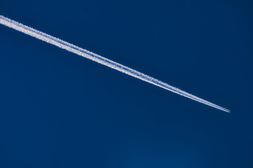 Airplane flying high in blue sky leaving white contrail trail behind
