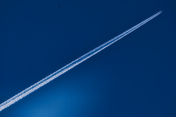 Airplane flying high in blue sky leaving white contrail trail behind