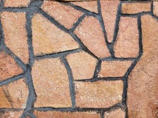 Close-up of natural stone wall texture with irregular brown tiles and dark grout lines. Decorative masonry background for construction, design, and architecture.