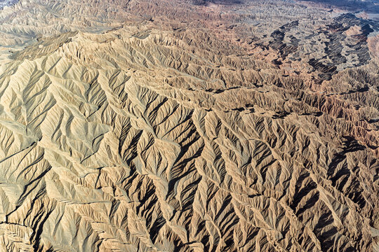 Aerial view of the stark, textured landscape of Huoyun Valley, carved by time and elements, with its deep shadows contrasting against the sun-baked earth, Huoyun Valley, China.