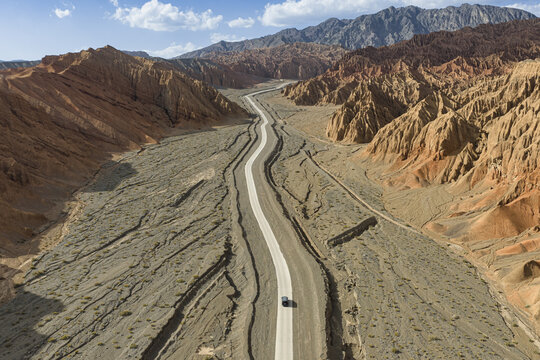 Aerial view of a sinuous road cutting through the rugged terrain of Huoyun Valley, where fiery red rock formations meet the stark desert floor, Huoyun Valley, China.