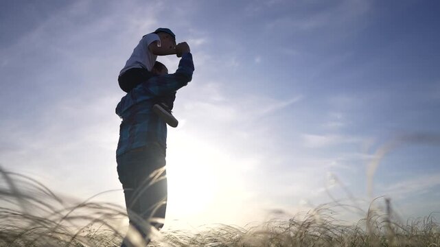 Father and son in a field. Father and child playing in the grass outside at sunset. Silhouette of happy happy bonding in the sky. A dad and his son in a meadow lifestyle.