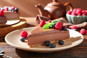 Piece of tasty chocolate cheesecake with berries served on wooden table, closeup