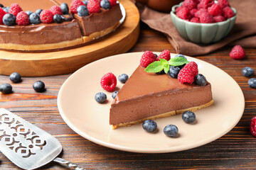 Piece of tasty chocolate cheesecake with berries on wooden table, closeup