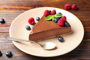 Piece of tasty chocolate cheesecake with berries on wooden table, closeup