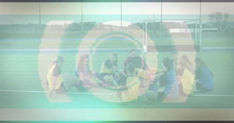 Female field hockey players sitting tight circle on turf, tapping ball initiating training drill - Powered by Adobe
