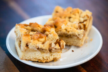 Two golden apple crumble bars rest on a white plate, showcasing layers of spiced apple filling and buttery crumb topping against a dark wooden background.