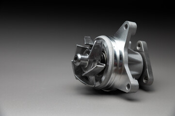 A new, shiny aluminum engine coolant pump on a gray gradient background. Contrast backlighting.