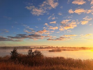 Fototapeta premium Golden sunrise with morning mist, soft blue skies, and a forest in the background. Peaceful and dreamy natural scene perfect for seasonal, landscape, or atmospheric visuals.