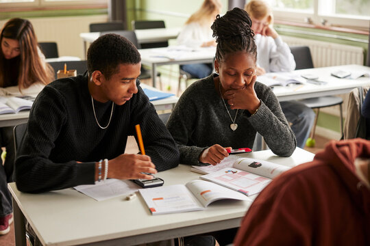 Teenage girl studying with male friend while sitting at desk in classroom at junior high school