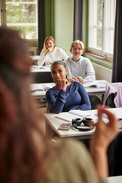 Portrait of smiling teenage female student listening to teacher while sitting in classroom attending lecture at school
