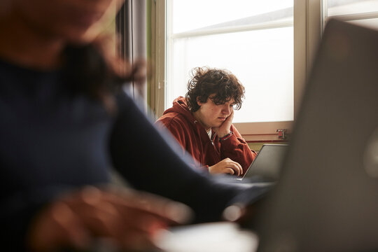 Teenage boy with tousled hair using laptop while studying in classroom at school