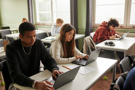High angle view of teenage girl and boy studying on laptop while sitting in classroom at junior high school