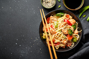 Asian noodles with chicken and vegetables at black background.