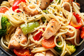 Stir fry chicken with vegetables and noodles at black background.