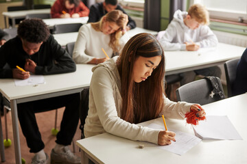 High angle view of teenage girl with Autism Spectrum Disorder squeezing stress ball while writing educational exam in sc