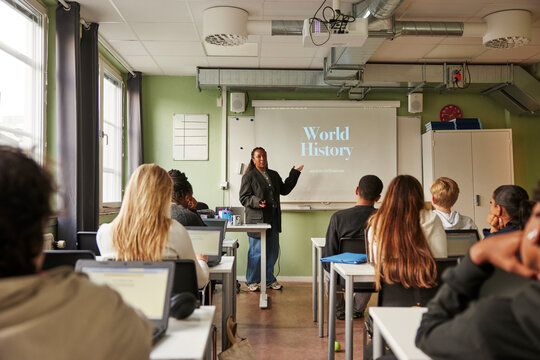 Female professor teaching about world history on projection screen to junior high students in classroom