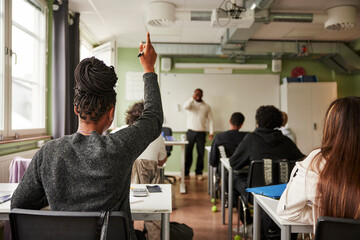 Rear view of teenage female student with hand raised during Q and A session in classroom