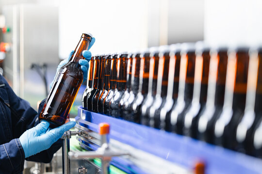 Worker hold Brown glass alcohol bottles. Automated beer bottling process in modern brewery factory