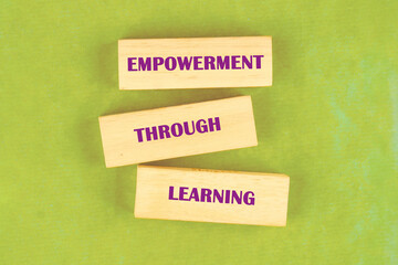 Through education and learning to success concept. EMPOWERMENT THROUGH LEARNING words assembled from blocks on a light green background, top view