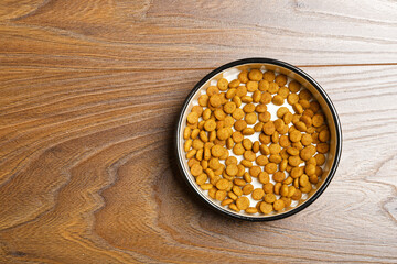 A bowl with a cat's dry food on a wooden floor. Top view.
