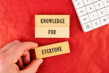 Learning for Everyone concept. Words KNOWLEDGE FOR EVERYONE assembled from blocks in a composition with part of a white calculator and a hand, top view
