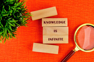 knowledge and education concept. KNOWLEDGE IS INFINITE assembled from wooden blocks in composition with magnifying glass and green plant on orange background, top view
