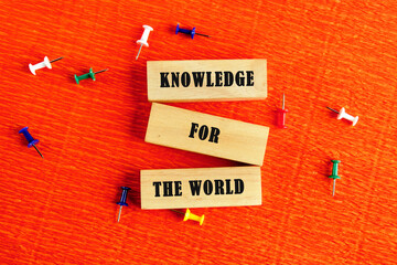 Business, success, idea, learning, planning, Education concept. KNOWLEDGE FOR THE WORLD assembled from wooden blocks in a composition with stationery pins on an orange provocative background, top view