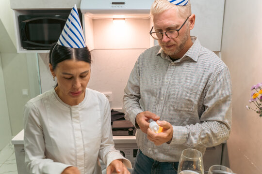 Couple Kitchen Party: Birthday celebration; cooking; preparing food indoors; happy couple wearing party hats.