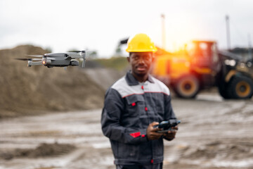 Portrait worker African male engineer utilizing uav drone for sand quarry mining control and...