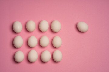 Top view of white chicken eggs arranged in a grid on a pink background with one egg apart. Minimal...
