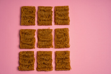 Flat lay of dry instant ramen noodle blocks scattered on a pink background. Minimalist composition with wavy texture, Asian cuisine concept, soft pastel lighting.