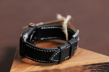 Black leather smartwatch band with white stitching on wooden surface