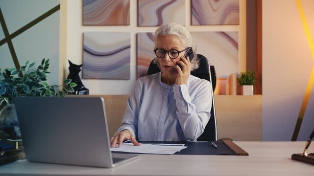 Annoyed senior businesswoman talking on phone with employee about performance