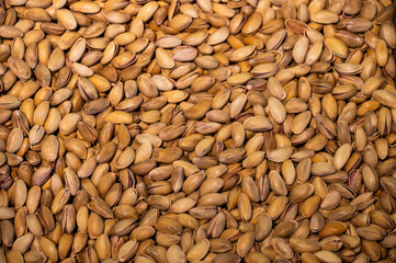 A large pile of unpeeled pistachios, hundreds of them. Close-up