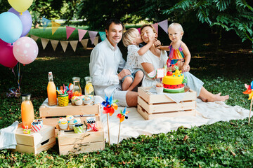 Family celebrating child's birthday outdoors. Birthday party with birthday cake and decorations.