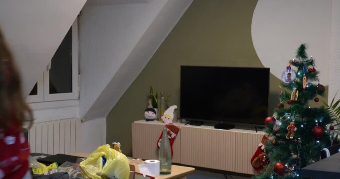 Teenager wearing Christmas clothes decorates the house for Christmas. Walks in front of the camera. Medium shot.