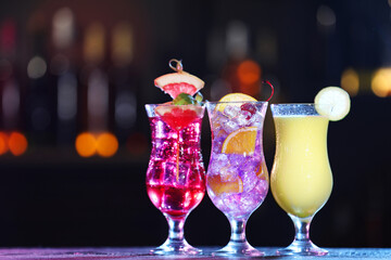 Glasses of alcoholic cocktails with garnish on table against blurred background, space for text